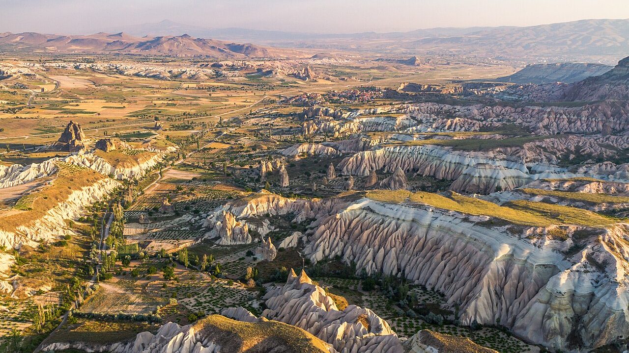 Kapadokya'da gün doğumunda gökyüzünde süzülen sıcak hava balonları ve tarihi peribacaları manzarası